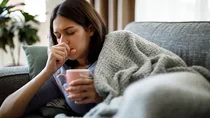 Eine kranke Frau liegt auf dem Sofa und hustet. 