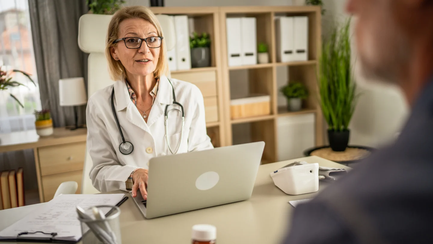 Eine &Auml;rztin unterh&auml;lt sich mit ihrem Patienten. Dabei tippt sie etwas am Computer.