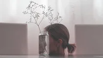 Das Gesicht einer Frau spiegelt sich verkehrt in einer Vase.