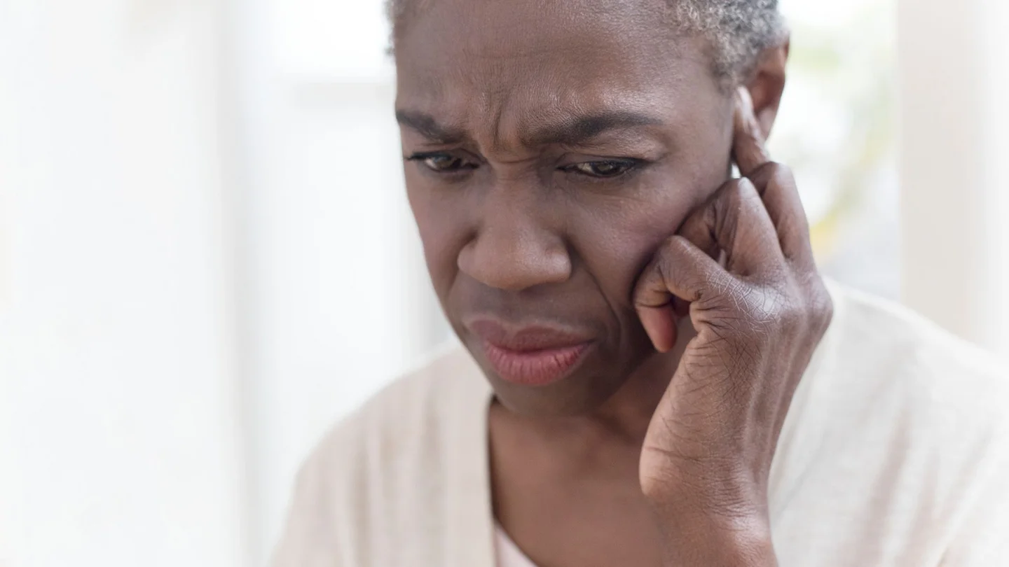 Tinnitus: Eine Frau fasst sich mit einem Finger ans Ohr und schaut skeptisch.