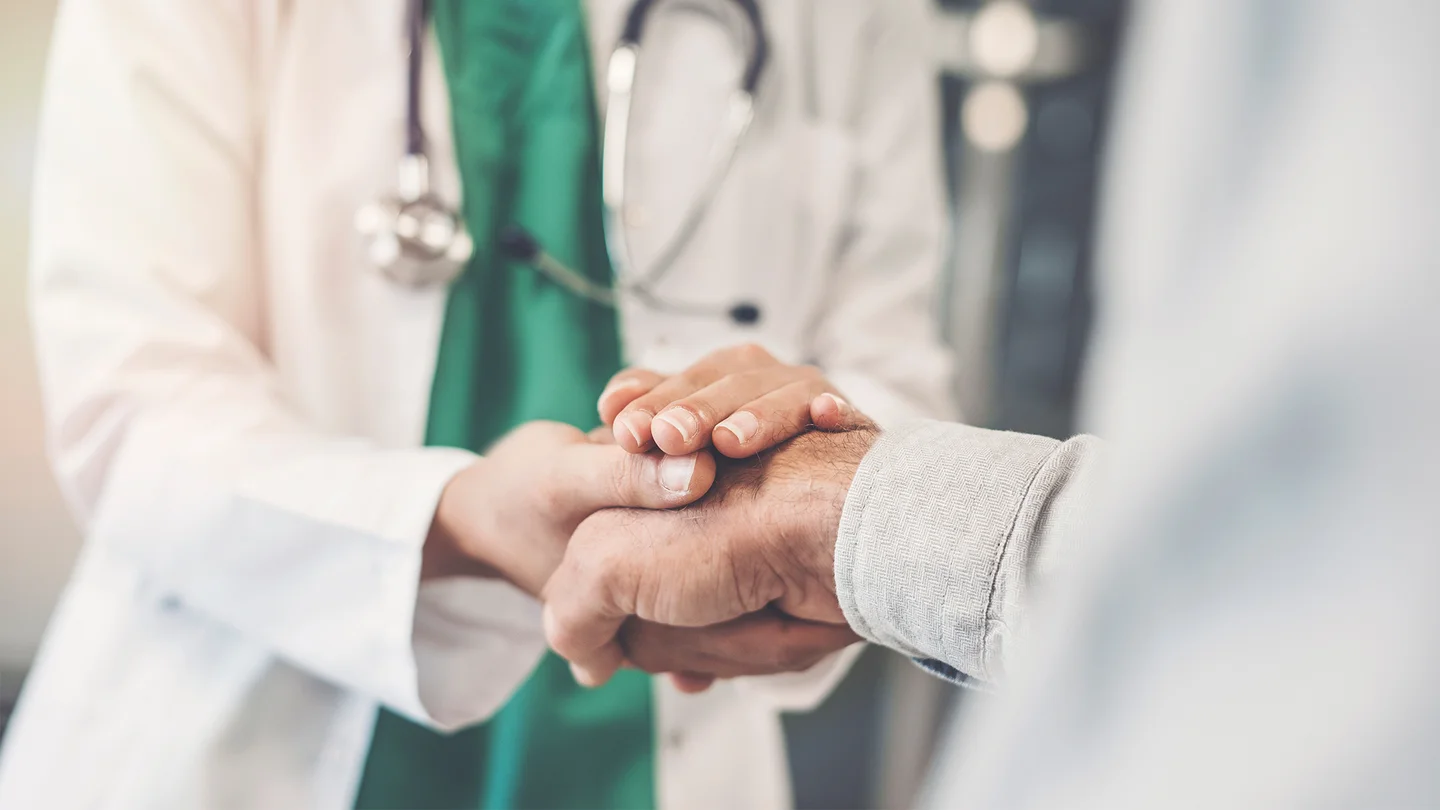 Bauchspeicheldrüsenentzündung: Ein Arzt umschließt mit beiden Händen die Hand eines Patienten.