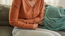 Hepatitis A: Eine Frau sitzt auf einem Sofa und h&auml;lt die Arme &uuml;ber dem Bauch. Sie hat Bauchschmerzen.
