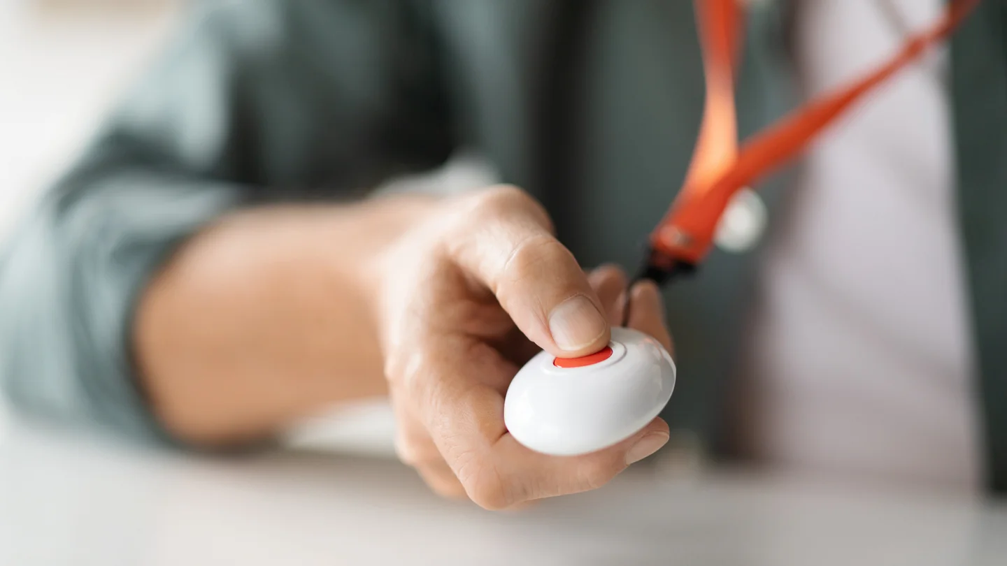 Eine Person drückt auf einen Knopf, den sie an einem Band um den Hals trägt.