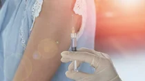 Eine Hand hält eine aufgezogene Spritze. Im Hintergrund ist der Arm einer Frau zu sehen.