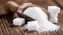 Zucker: Eine Holzschaufel ist mit Zuckerkristallen bef&uuml;llt. Rechts und links neben der Schaufel liegen mehrere Zuckerw&uuml;rfel