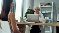 Eine Frau sitzt in einem Behandlungszimmer. Ihr gegen&uuml;ber sitzt eine &Auml;rztin und guckt auf ihren Laptop.