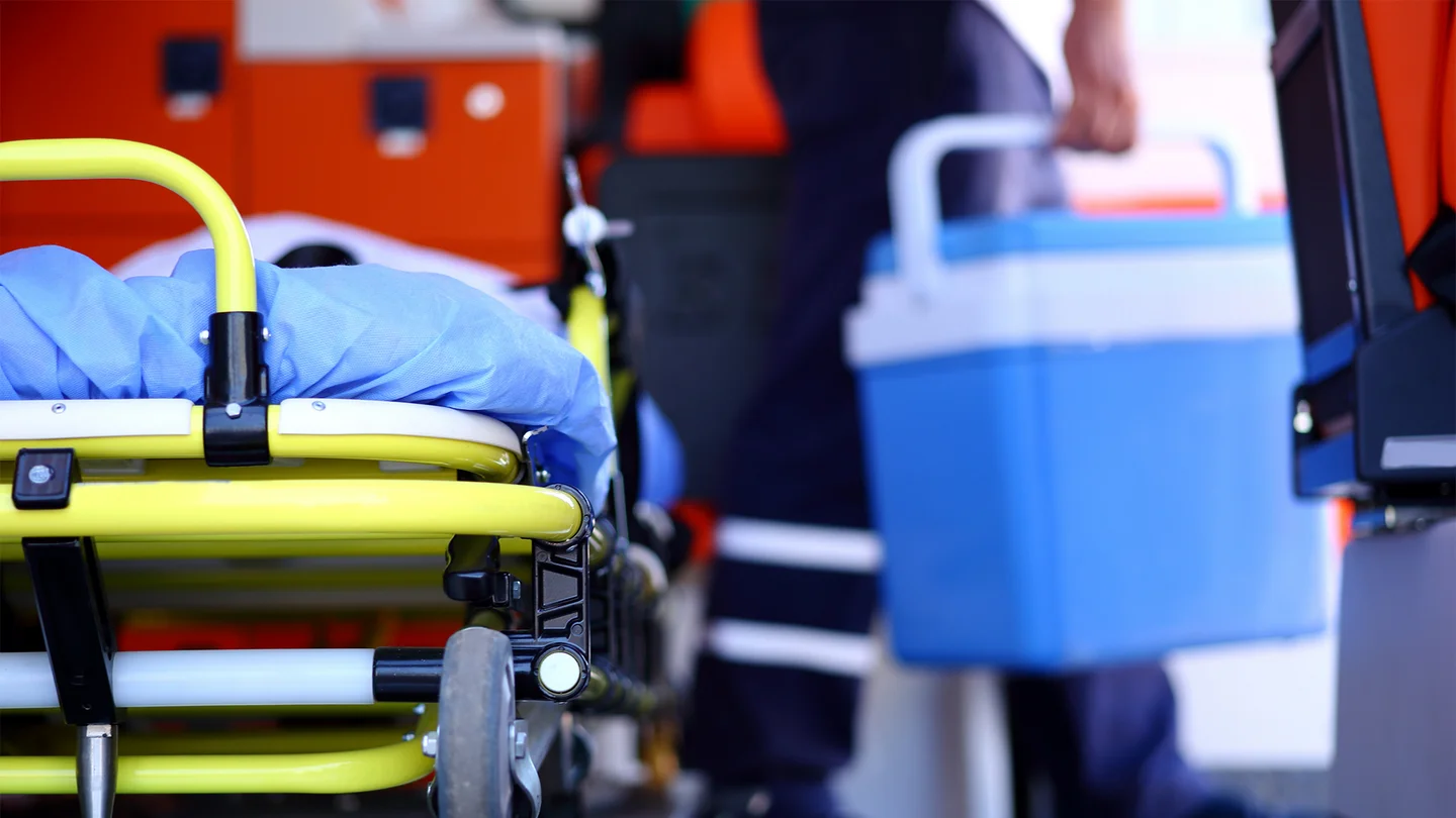 Organspende: Im Vorgergrund ist eine mobile Krankentrage zu sehen. Unscharf und im Hintergrund tr&auml;gt eine Person einen K&uuml;hlbeh&auml;lter f&uuml;r Transplantationsorgane.