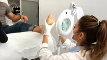 Ein Mann sitzt auf einem Behandlungsstuhl und streckt ein Bein nach vorne. Eine Ärztin trägt Stickstoff auf eine Warze am Fuß auf.