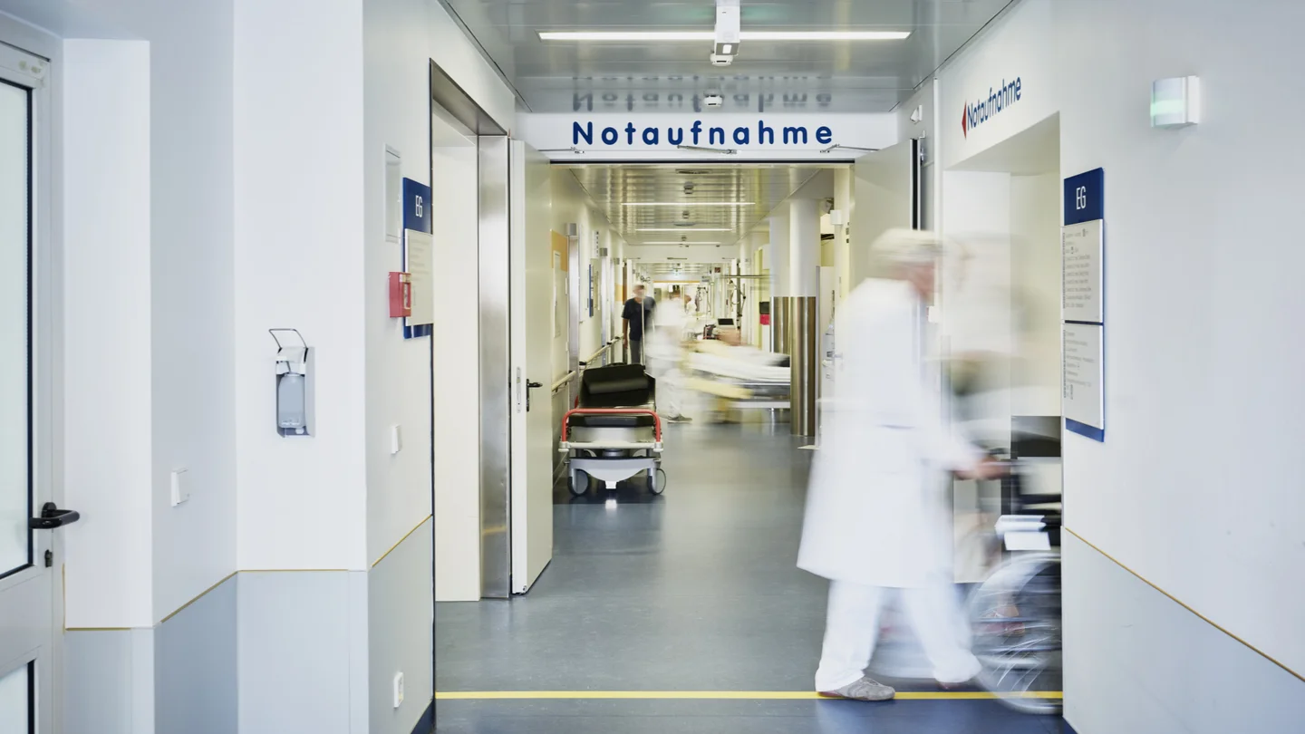 Krankenhauspersonal schiebt einen Patienten im Rollstuhl über den Gang der Notaufnahme