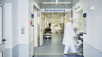 Krankenhauspersonal schiebt einen Patienten im Rollstuhl über den Gang der Notaufnahme